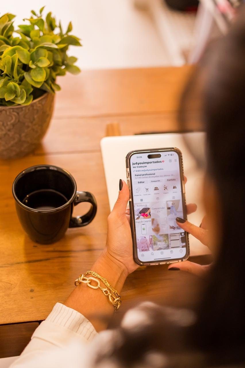 Mãos segurando um celular com o perfil da Ju4You no Instagram